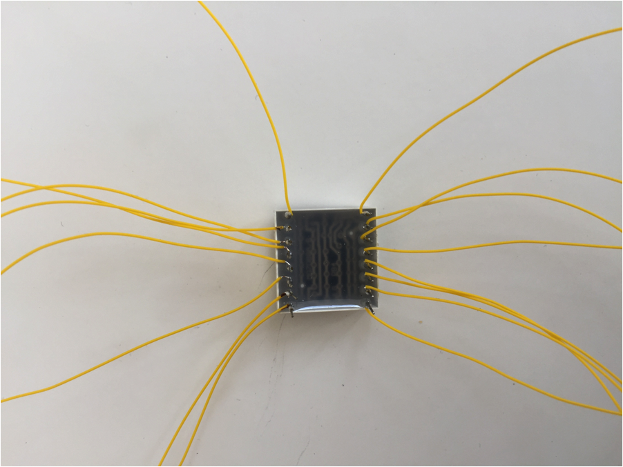 LED matrix component viewed from the bottom, with a yellow wire wrapped and soldered to each pin